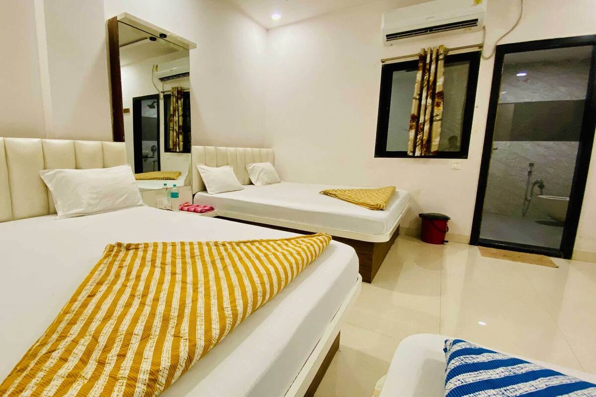A hotel room with a large bed, a smaller bed, a bathroom with a shower, and a mirror.