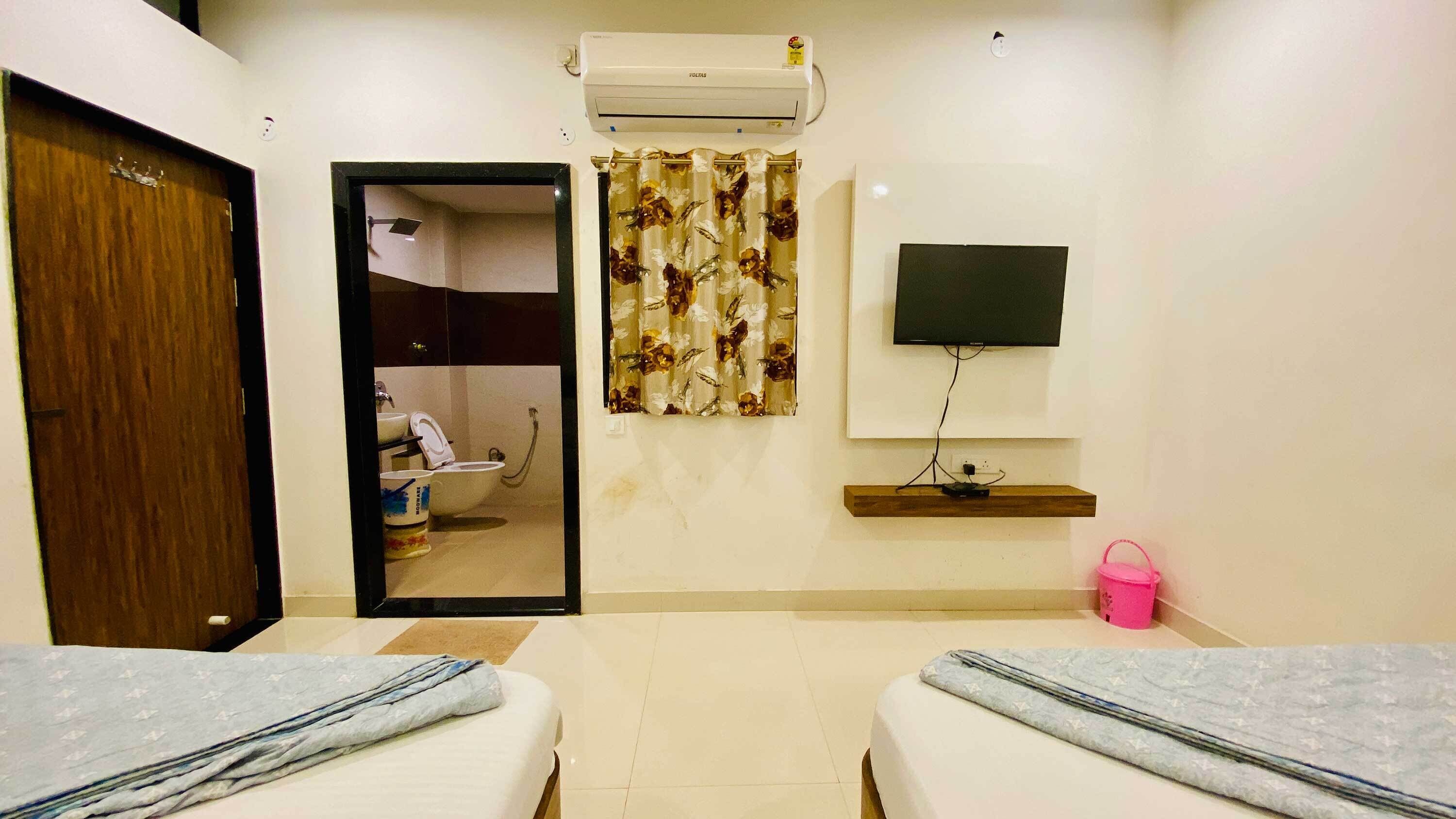 A hotel room with two beds, a TV, an air conditioner, a shower, and a bathroom mirror.