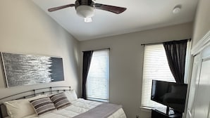 A bedroom with a bed, a ceiling fan, a TV on a stand, and a painting on the wall.