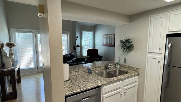 A modern kitchen with granite countertops, white cabinetry, and a stainless steel refrigerator.