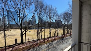 A balcony with a view of a park, a road, and buildings in the distance.