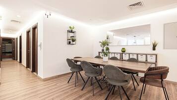A modern meeting room with a wooden table and grey upholstered chairs, white walls, and a wooden floor.