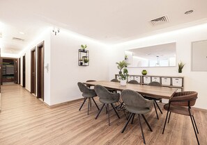 A modern meeting room with a wooden table and grey upholstered chairs, white walls, and a wooden floor. - Next'House - Business Boulevard Hostel (Dubai)