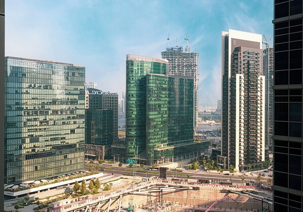 A cityscape with modern high-rise buildings, including a prominent glass skyscraper and a construction site. - Next'House - Business Boulevard Hostel (Dubai)