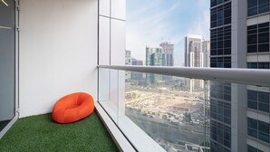 A balcony with a green artificial turf, a white railing, and an orange bean bag chair. - Next'House - Business Boulevard Hostel (Dubai)