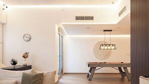 A modern living room with a sofa, a coffee table, a clock, and a pool table. - Next'House - Business Boulevard Hostel (Dubai)