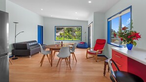 Ein moderner Wohnraum mit Essbereich, einem roten Sessel, einem blauen Sofa und Blick auf Grün durch große Fenster.