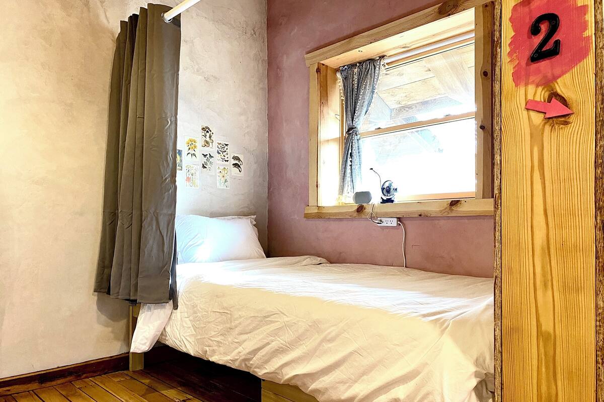 A small, single-bed room with a wooden floor, a window with curtains, and a wall-mounted number '2'.