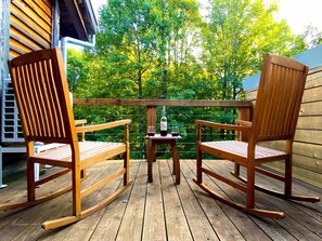 Una terraza de madera con dos mecedoras y una mesita con una botella y un vaso.