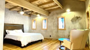 A bedroom with a wooden bed, a chair, and a small table. There are windows with curtains and a ceiling fan. - Arete Hostel (Summersville)