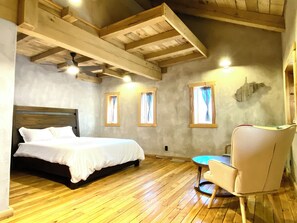 A bedroom with a wooden bed, a chair, and a small table. There are windows with curtains and a ceiling fan. - Arete Hostel (Summersville)