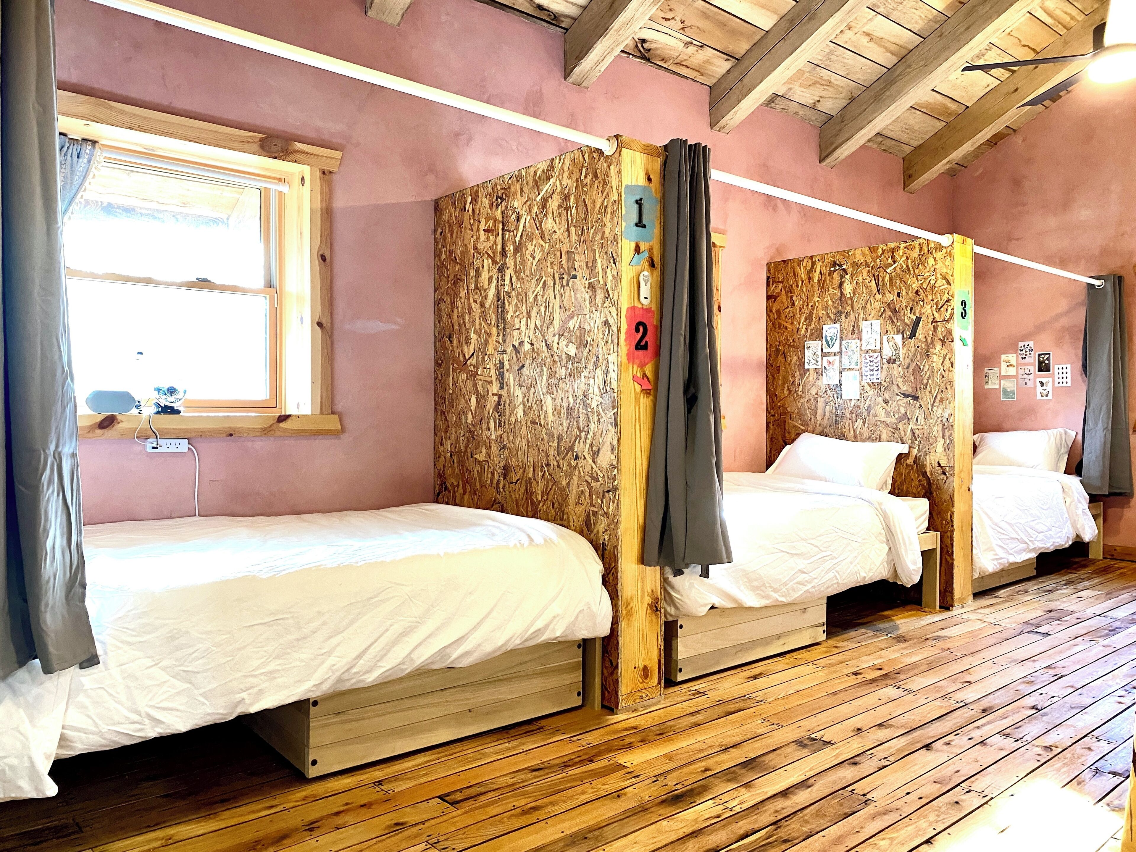 A room with two wooden bunk beds, a window with curtains, and a wooden floor.