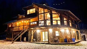 A multi-level wooden cabin with large windows, a stone foundation, and a wooden deck. - Arete Hostel (Summersville)