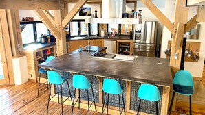 A modern kitchen with a central island, bar stools, stainless steel appliances, and wooden beams. - Arete Hostel (Summersville)