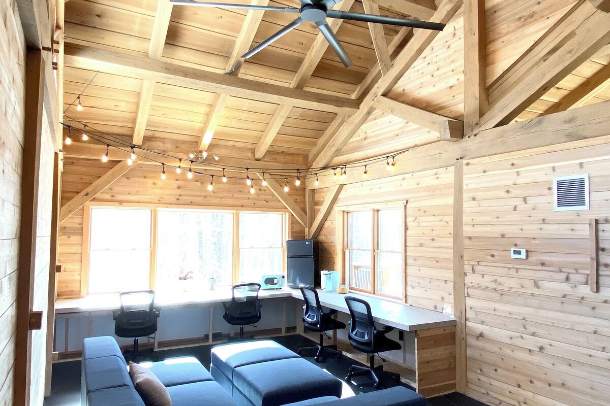 A cozy cabin interior with a wooden ceiling, a ceiling fan, a dining area with a table and chairs, and a large window providing natural light.