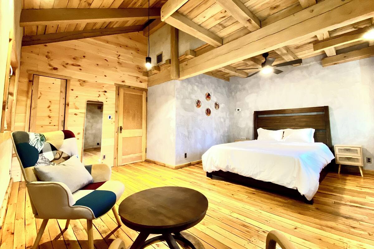 A wooden-floored bedroom with a bed, a chair, a small table, and a ceiling fan.