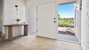 Una stanza con parete in mattoni bianchi, una panca di legno, una porta con vista e un lampadario.