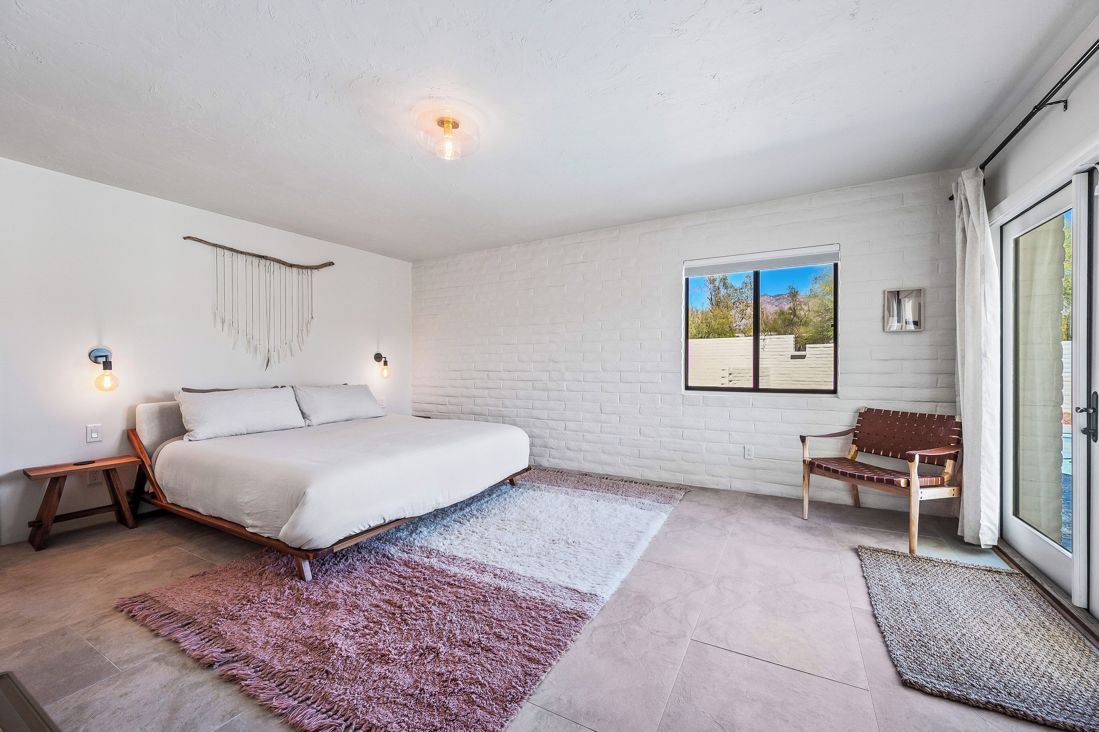 Een slaapkamer met een bed, een bankje, een raam en een deur.