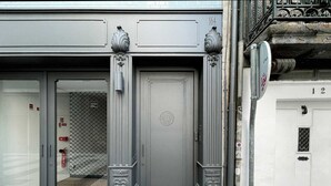 Une entrée d’immeuble avec une porte grise, un portail en métal et un extincteur fixé au mur.