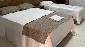 Habitación de hotel con dos camas, cabecero de madera, mesita de noche, una pequeña mesa con una toalla y un equipo de aire acondicionado.