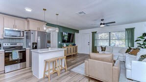 A modern kitchen with a central island, wooden bar stools, a white sofa, and a ceiling fan. - Beautifully Decorated Largo Home,  close to beaches, Pinellas Trail & Johns Lake (Largo)