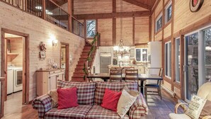 Un intérieur de chalet chaleureux avec un escalier en bois, un coin repas et une cuisine.