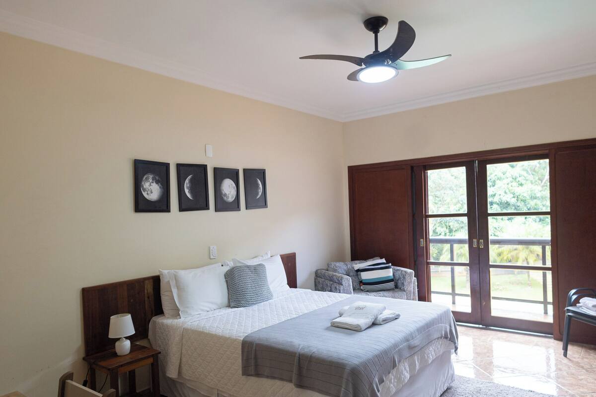 Ein Schlafzimmer mit Bett, Schreibtisch, Stuhl, Deckenventilator und einer Schiebetür zu einem Balkon.