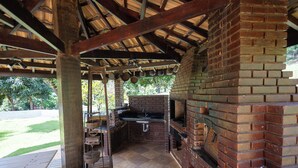 An outdoor kitchen with a brick oven, a sink, and a grill. - Pousada Costa Rielli (Águas de Lindóia)