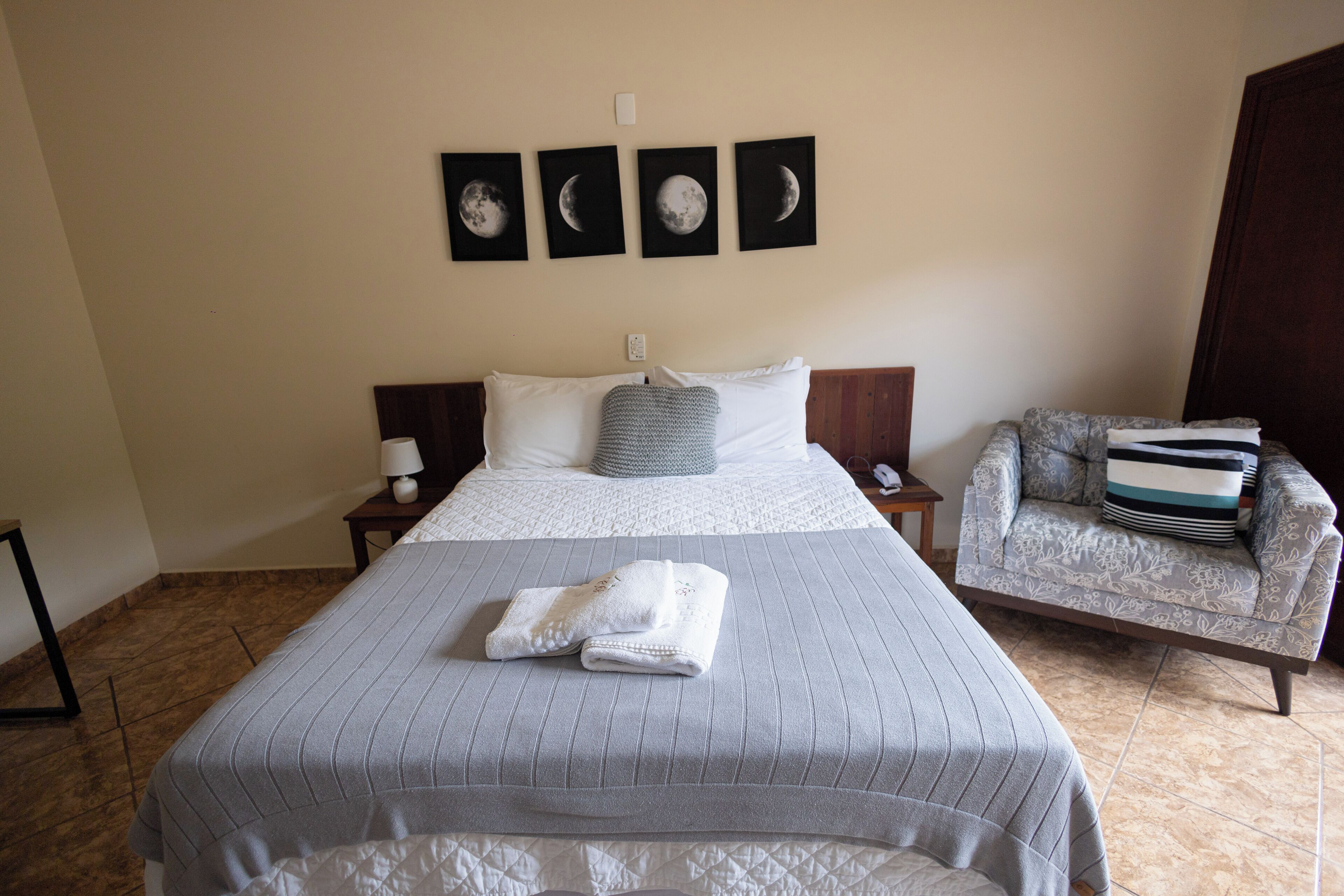 A hotel room with a large bed, a chair, and four moon phase wall art.