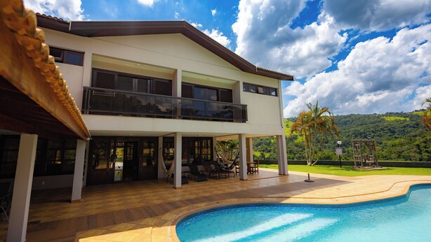A two-story house with a swimming pool, covered patio, and a view of the surrounding landscape. - Pousada Costa Rielli (Águas de Lindóia)