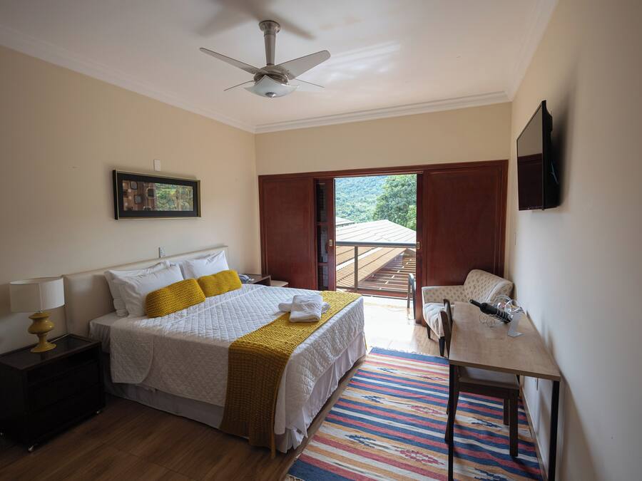 A bedroom with a bed, bedside table, lamp, and a television on the wall.