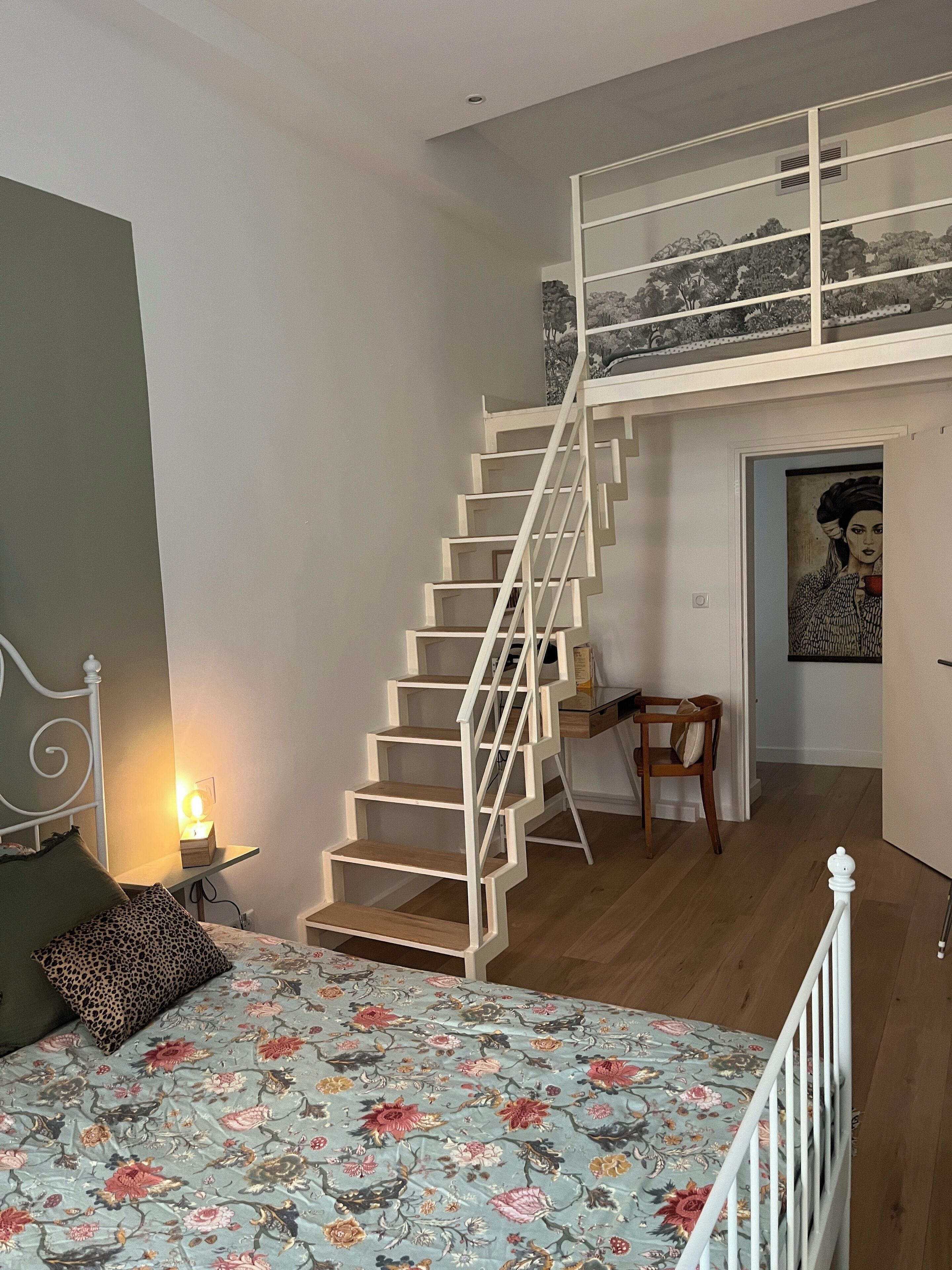Ein Schlafzimmer mit einem Bett, einem Nachttisch, einer Lampe, einer Treppe und einem Schreibtisch.
