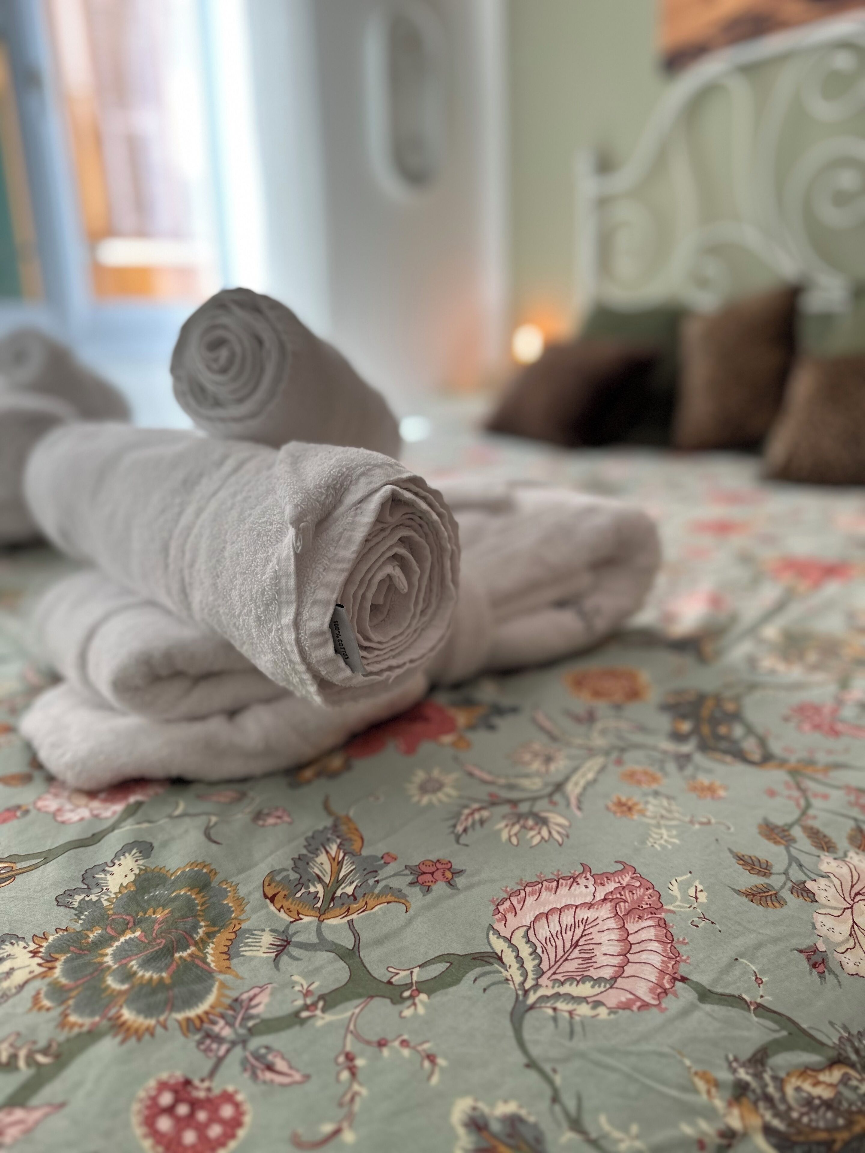 Una cama con toallas enrolladas y un edredón estampado con motivos florales.