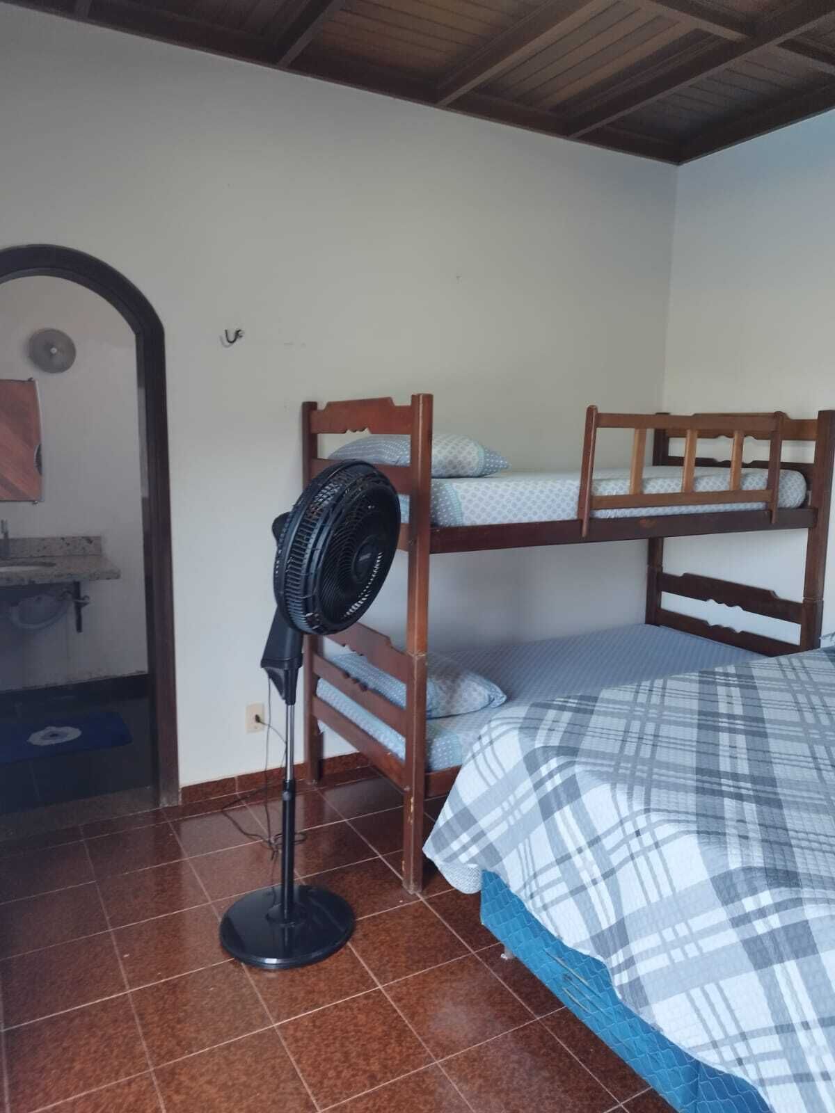 A room with two bunk beds, a standing fan, and a tiled floor.