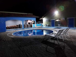 Una piscina exterior con diseño curvo, rodeada por una zona cubierta con asientos y un pequeño bar.