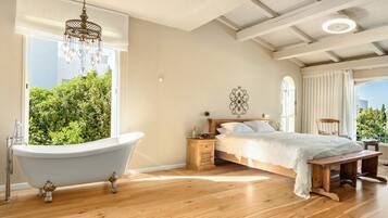 A bedroom with a large window, a bathtub, a bed with a white bedspread, and a wooden bench.