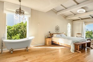 Ein Schlafzimmer mit großem Fenster, einer Badewanne, einem Bett mit weißer Bettdecke und einer Holzbank.