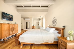A bedroom with a wooden bed, a wooden nightstand, a TV mounted on the wall, and a decorative wall piece.