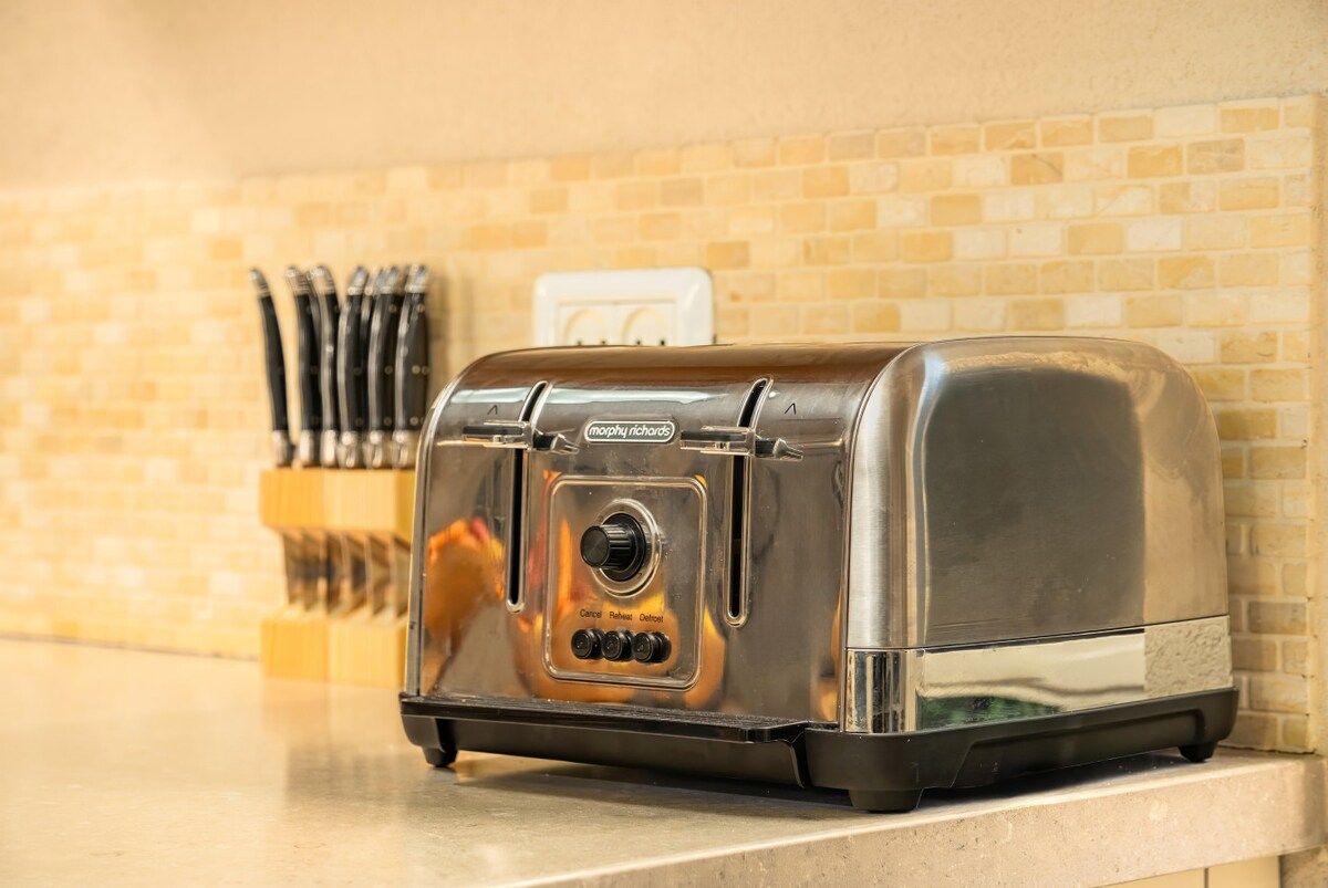 A toaster on a kitchen counter with a brick wall in the background.