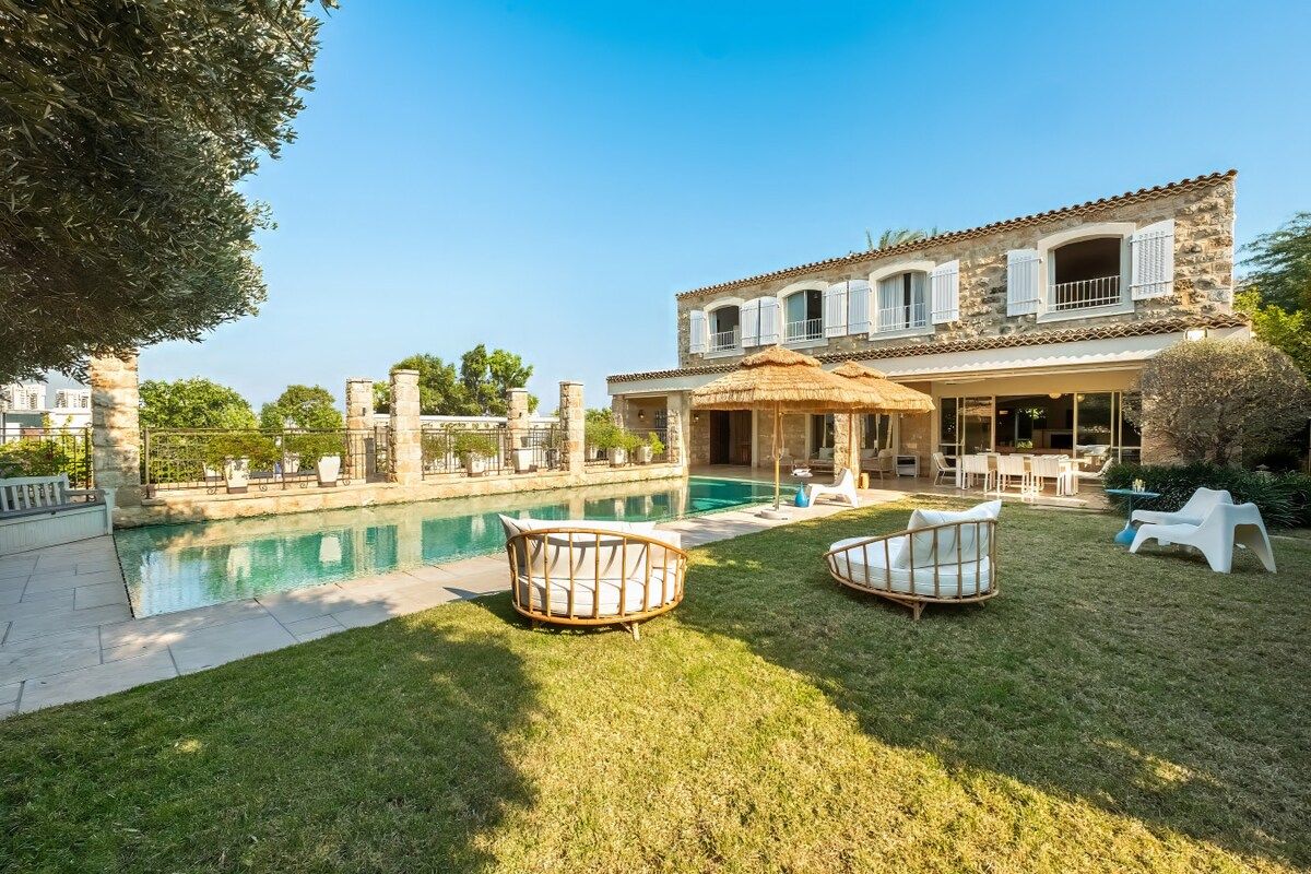 Un espace aménagé au bord de la piscine, avec un bâtiment en pierre, du mobilier d’extérieur et un ciel dégagé.