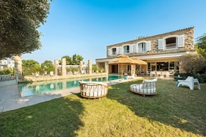 A poolside area with a stone building, outdoor furniture, and a clear sky.