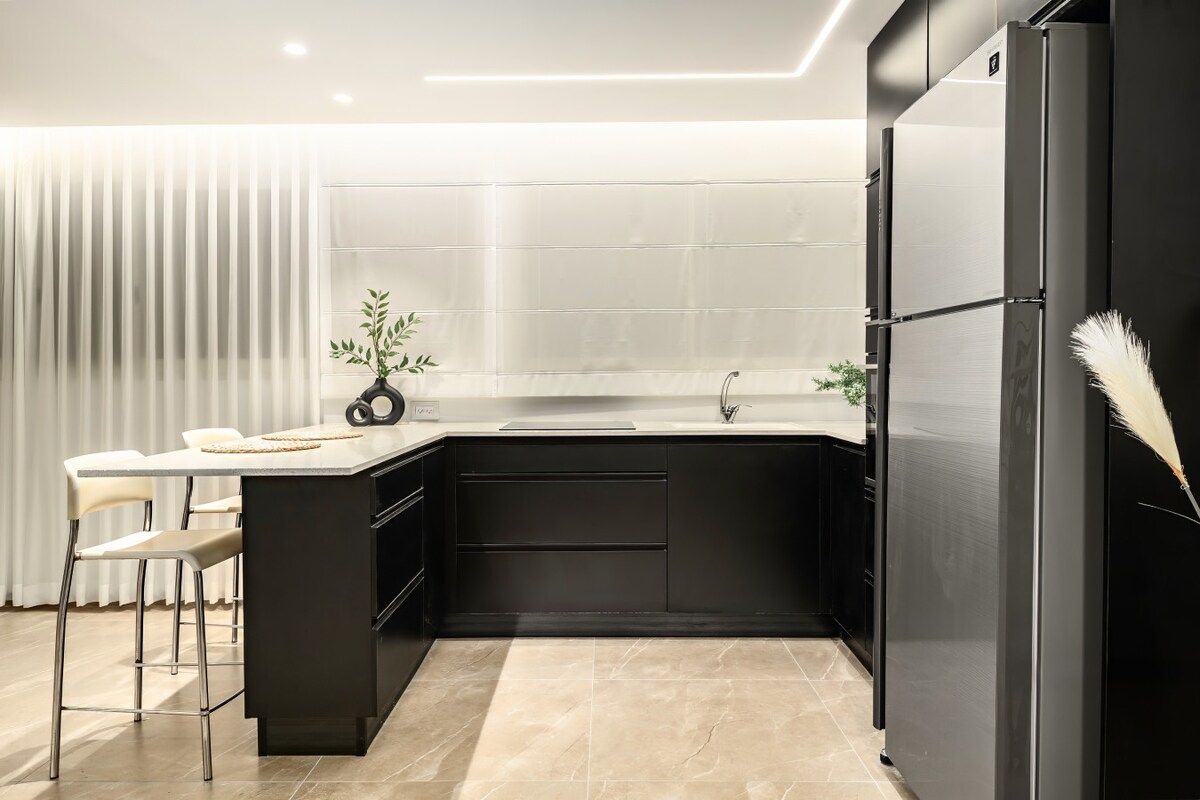 A modern kitchen with a black countertop, stainless steel appliances, and a bar stool.