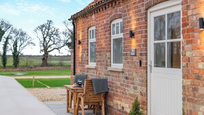 A brick house with a white door and windows, a small table with chairs, and a potted plant outside. - The Stables - UK46003 (Cranswick, near Driffield)