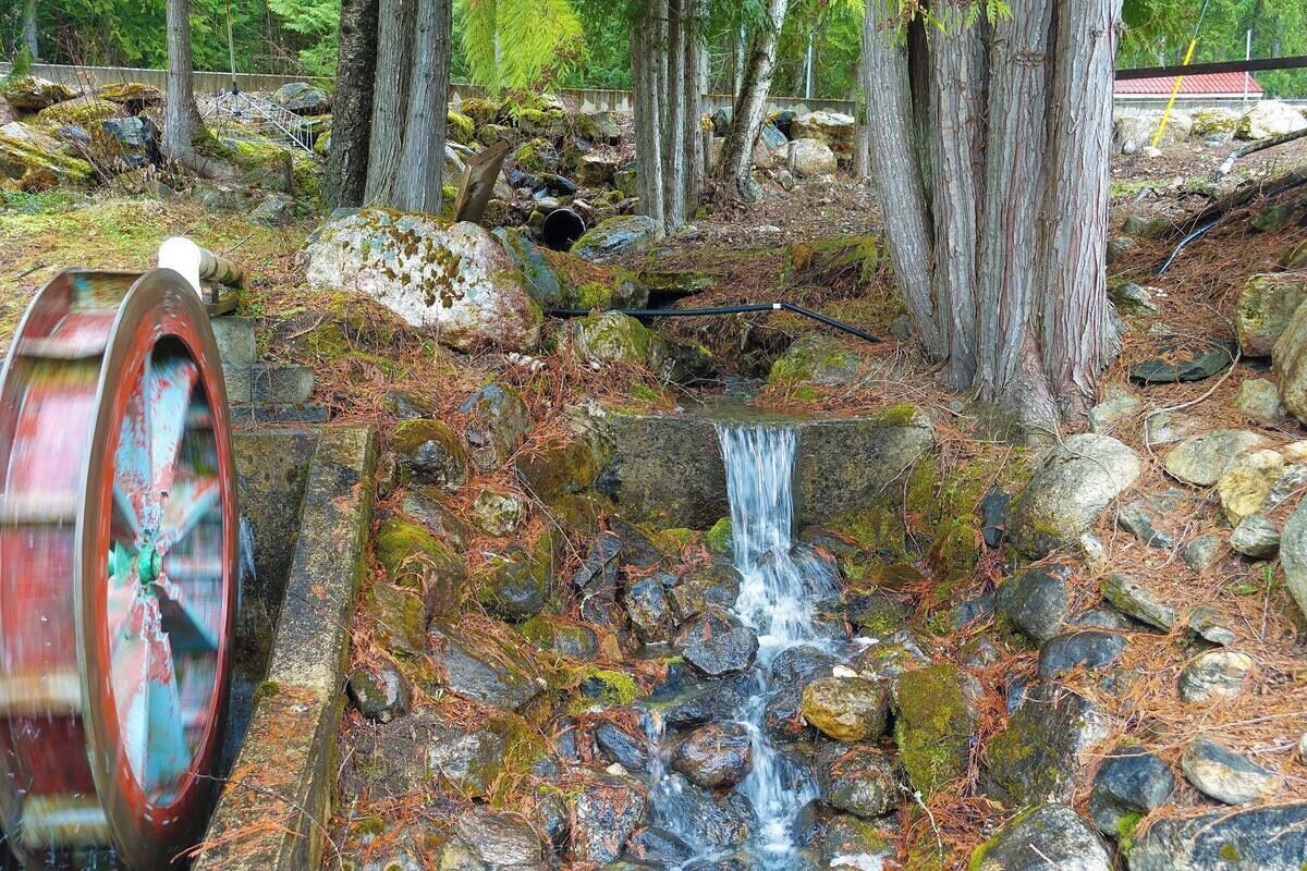 A waterfall in a forested area with a large metal wheel structure nearby.