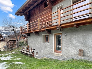 A wooden house with a balcony, stone walls, and a wooden fence.