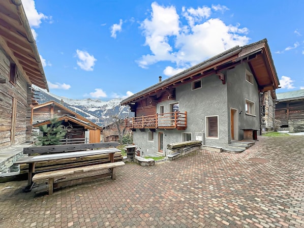 A rustic building with a balcony, wooden benches, and a paved courtyard.