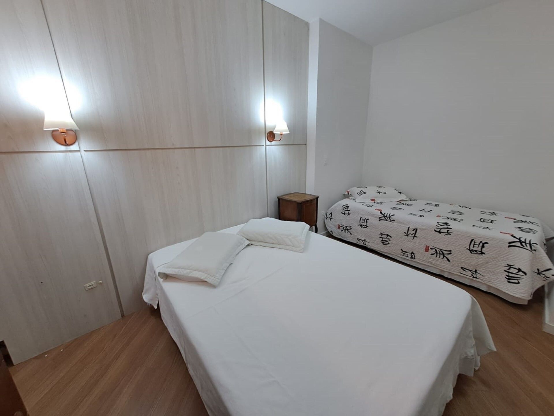 A room with a bed, a bedside table, and a wall-mounted lamp.