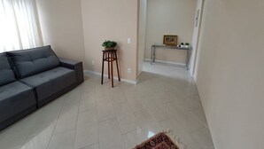 Een woonkamer met een bank, een klein houten krukje met een plant, een console tafel met een foto en een kamerbreed tapijt met een patroon.