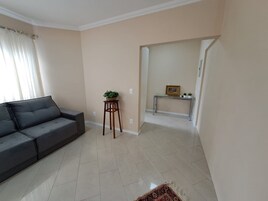 A living room with a sofa, a small wooden stool with a plant, a console table with a picture, and a patterned rug.