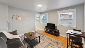 A living room with a sofa, coffee table, TV stand, dining table, and chairs.